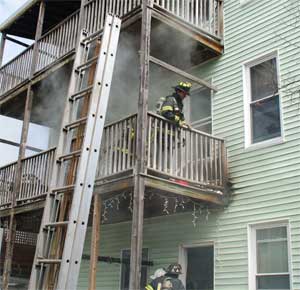 A ladder is raised as smoke envelopes Firefighter Mike Finnegan working on a rear porch of 68-70 Holland St. 